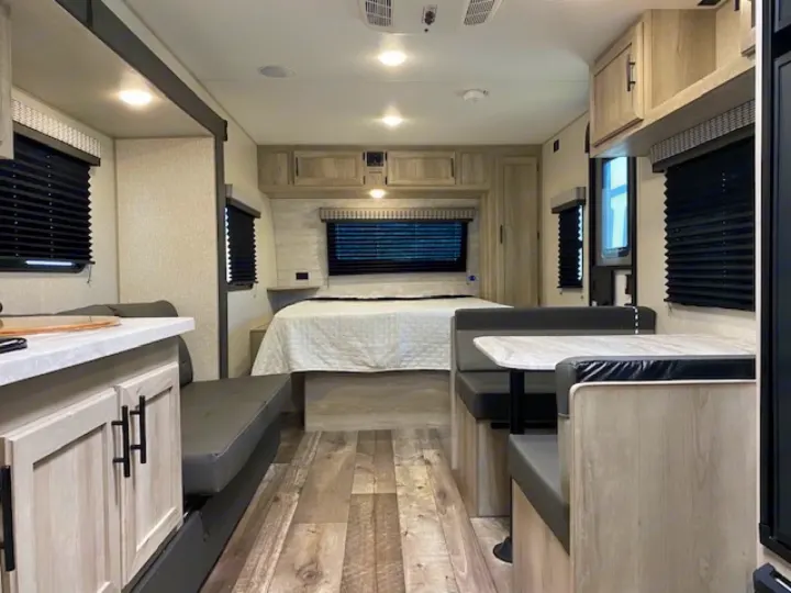 Bright RV rental interior: bed, dinette, and kitchen counter with light wood, creating a spacious and comfortable layout.. Escape e231bh 2022