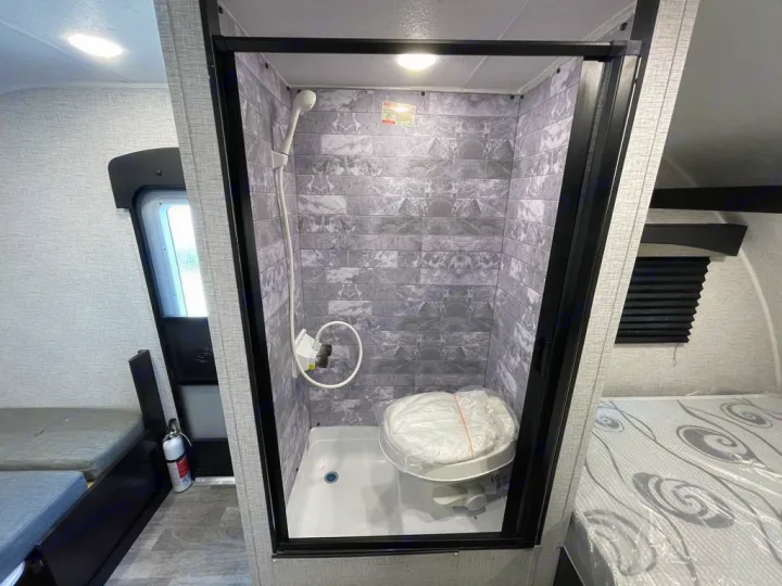 RV rental interior shows a compact wet bath with shower and toilet, flanked by bunk beds on the left and a main bed on the right.. Braxton Creek BUSHWHACKER PLUS 17FD 2022