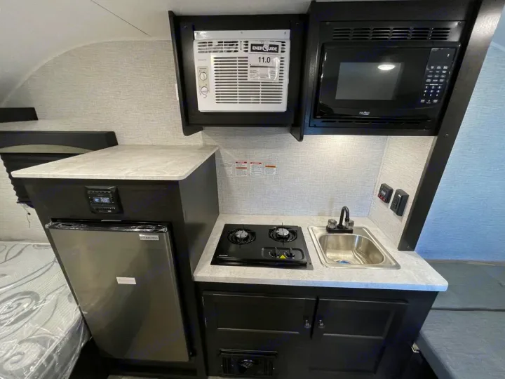 RV rental interior: Compact kitchen featuring a fridge, microwave, AC unit, sink, and two-burner cooktop.. Braxton Creek BUSHWHACKER PLUS 17FD 2022