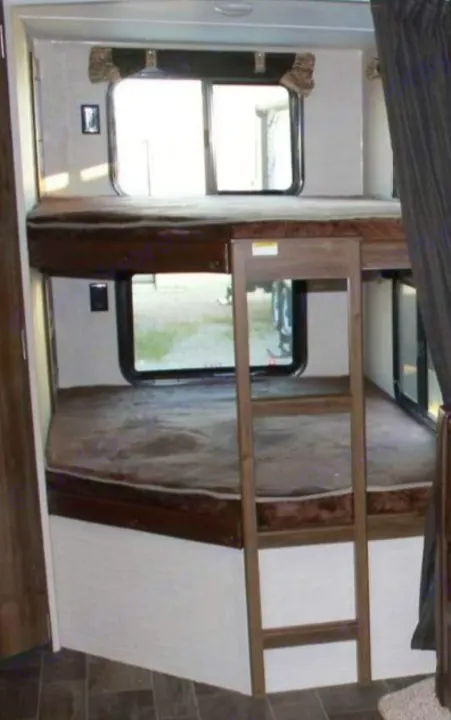 Inside an RV rental, comfortable bunk beds are shown with windows and a ladder, ready for family adventures.. Keystone RV Bullet Ultra Lite 2016