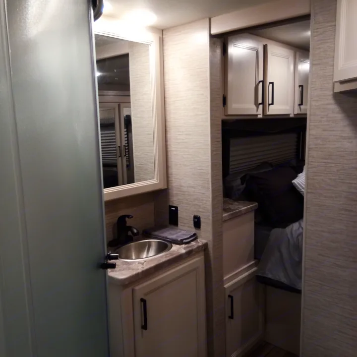 RV rental interior: compact bathroom with sink and mirror, adjacent to a cozy bedroom with overhead cabinets.. Thor Four Winds 2022
