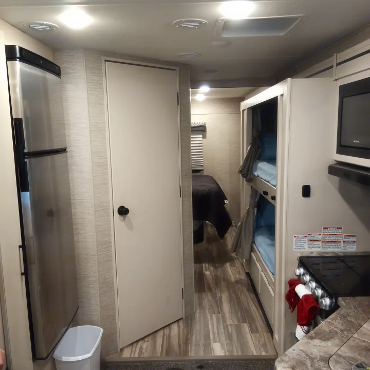 Inside an RV rental, highlighting the kitchen with fridge, bunk beds, and entry to the master bedroom for comfortable travel.. Thor Four Winds 2022