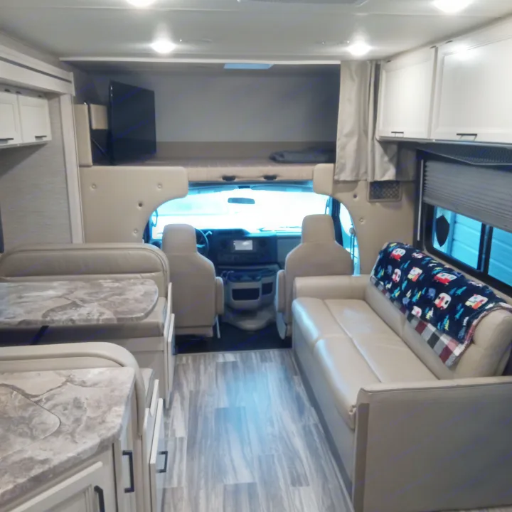 Experience the comfort of an RV rental with this inviting interior featuring a dinette, sofa, and over-cab bunk area.. Thor Four Winds 2022