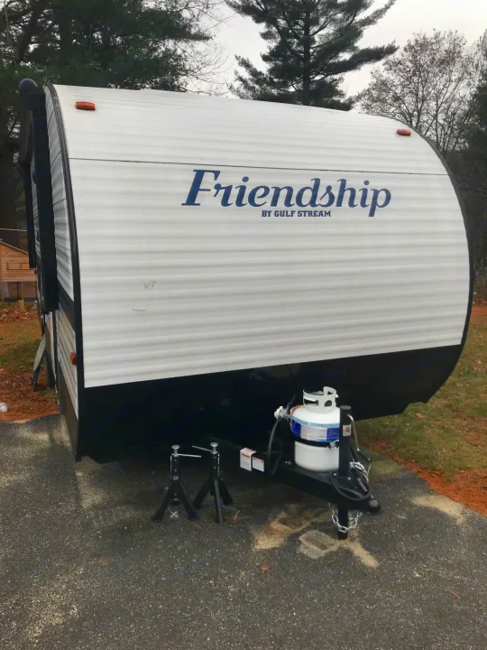 Front view of a white Gulf Stream travel trailer, an ideal rv rental. Features a propane tank and leveling jack stands.. Gulf Stream Friendship 2022