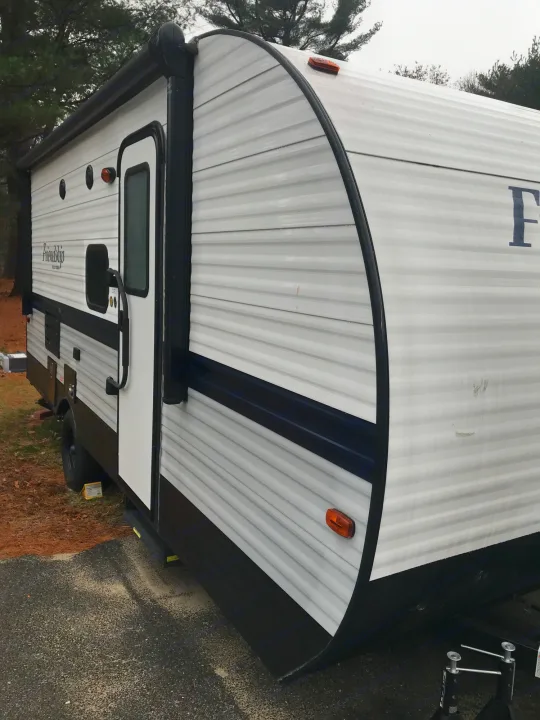 White travel trailer RV rental with a black base and blue stripe, parked outdoors. Features a side door and awning.. Gulf Stream Friendship 2022