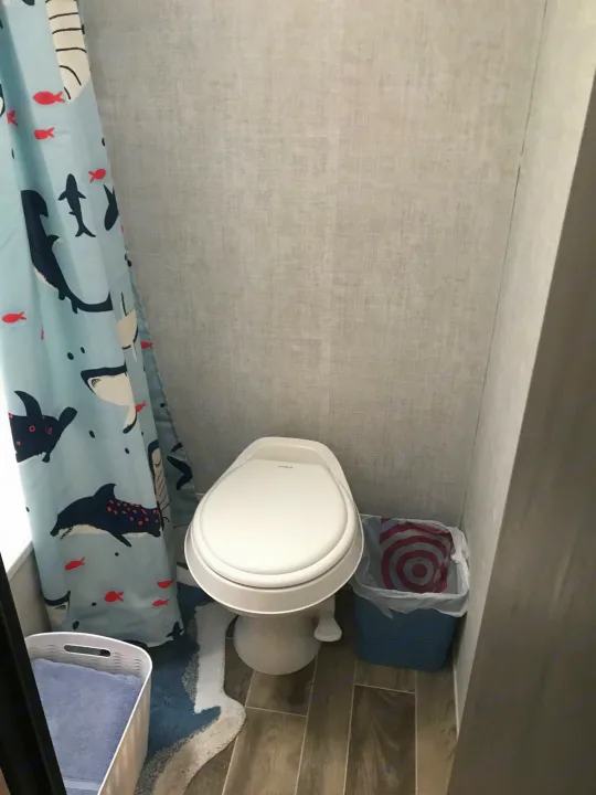 Compact RV rental bathroom: White toilet, shark shower curtain, and a blue bathmat. Functional space.. Gulf Stream Friendship 2022