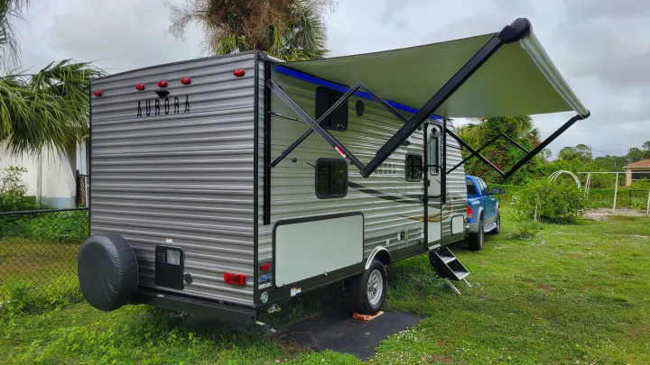 This **rv rental**, an Aurora travel trailer, is parked outdoors with its awning extended and blue LED lights illuminated.. Forest River Coachmen Aurora 2022