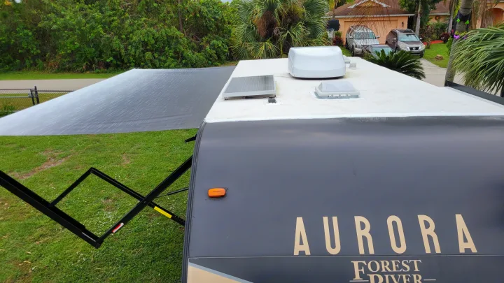 An RV rental, labeled 'Aurora Forest River', viewed from above, displays its extended gray awning, solar panel, and roof antenna.. Forest River Coachmen Aurora 2022