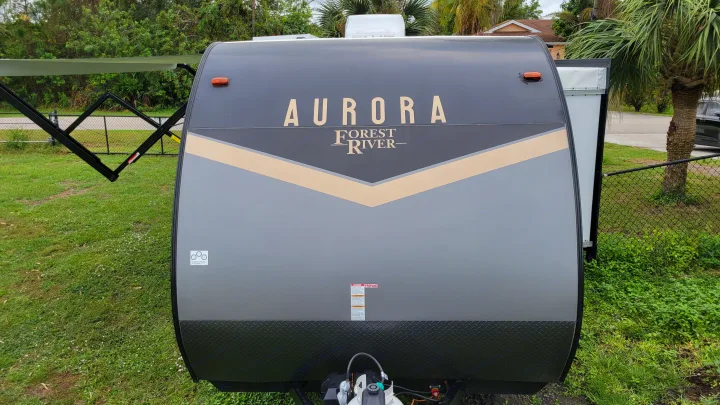 Front of a grey and beige Aurora Forest River travel trailer, perfect for an RV rental. Awning extended.. Forest River Coachmen Aurora 2022