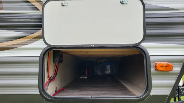 Open pass-through storage in an RV rental, revealing a charge controller, wiring, and ample space for travel gear inside.. Forest River Coachmen Aurora 2022