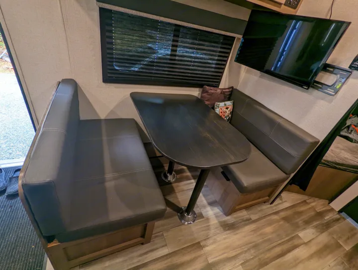 Inside an RV rental: a comfortable dinette with dark benches, a wood table, window blinds, and a mounted TV.. Highland Ridge RV Open Range 2022