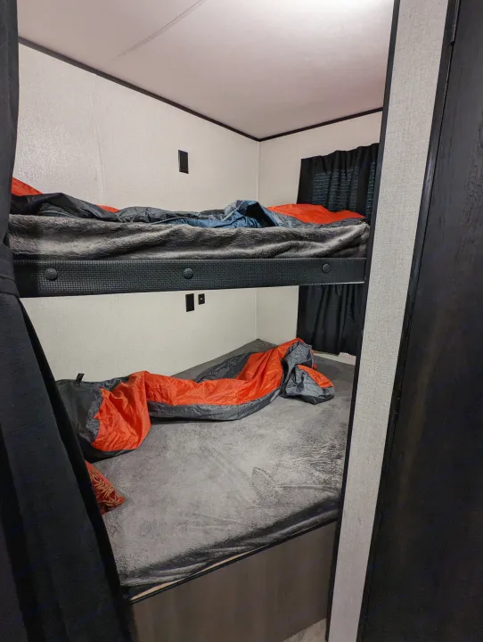 View of an RV rental's compact sleeping area, showing two bunk beds with a grey blanket on the upper and an orange sleeping bag on the lower.. Highland Ridge RV Open Range 2022