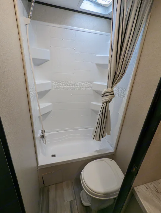 This RV rental bathroom features a white shower/tub combo with shelves, a striped curtain, and a modern toilet.. Highland Ridge RV Open Range 2022