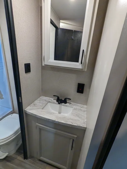 Compact RV rental bathroom featuring a sink, toilet, shower, and mirrored medicine cabinet. Ideal for your next RV adventure.. Highland Ridge RV Open Range 2022