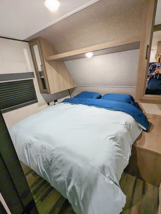An RV rental bedroom showcasing a bed with blue bedding, overhead cabinets, an emergency exit window, and a mirror.. Highland Ridge RV Open Range 2022