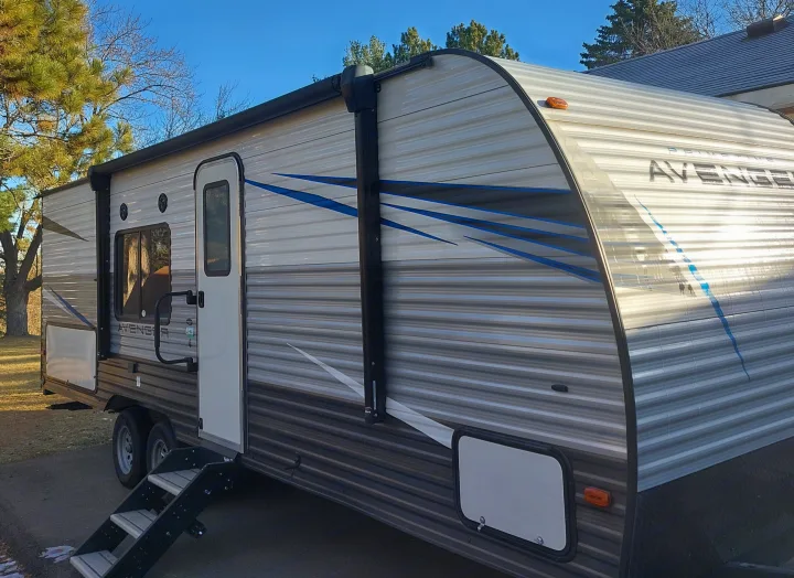 Get ready for adventure! Side view of a grey and white travel trailer (RV) with steps, awning, and door, ideal for rv rental.. Avenger Avenger Trailer 2021