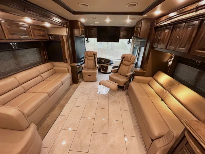 Explore this spacious luxury RV rental interior with plush beige sofas, captain's chairs, TV, and elegant wood cabinetry.. Phaeton Phaeton Motorhome 2017