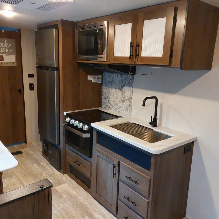 Modern RV rental kitchen and living space, featuring appliances, wood cabinets, and light flooring.. Avenger Avenger Trailer 2021