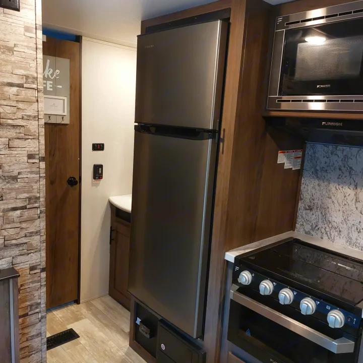 Modern RV kitchen with black and stainless steel microwave, stove, and a large refrigerator, great for your RV rental.. Avenger Avenger Trailer 2021