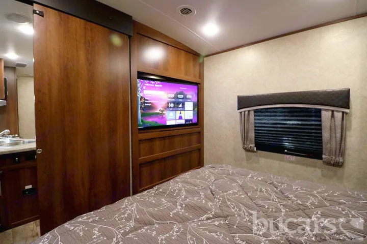 Comfortable RV rental bedroom featuring a large TV, cozy bed, and practical sliding door. Ideal for travel.. Jayco Eagle 2016