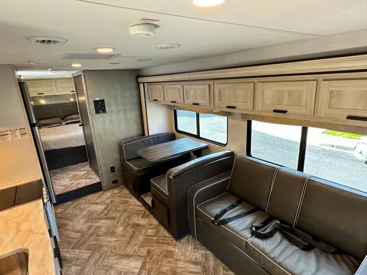 RV rental interior: Spacious living area with dining booth, sofa (with seatbelts), kitchen, and bedroom access.. Coachmen Sunseeker 2022