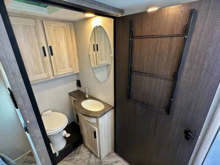 Inside an RV rental: a compact, modern bathroom with toilet, sink, mirror, cabinet, and towel rack.. Coachmen Sunseeker 2022