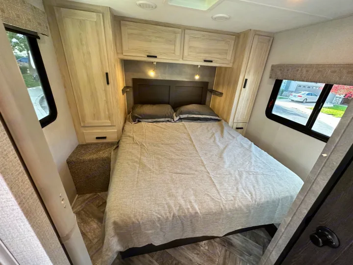 Cozy, modern RV rental bedroom with a comfy bed, overhead cabinets, and windows. Perfect for travel comfort.. Coachmen Sunseeker 2022