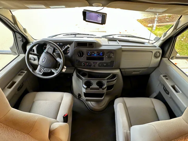Inside an RV rental: front cabin view with dashboard, steering wheel, comfortable seats, and backup camera monitor.. Coachmen Sunseeker 2022
