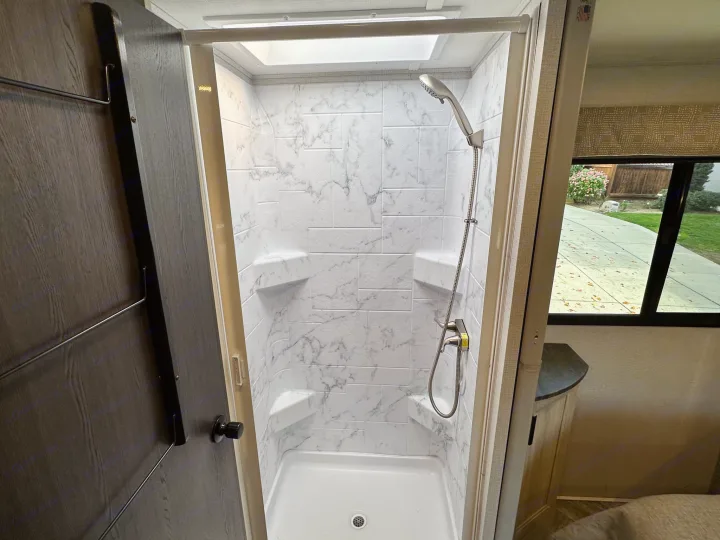 Spacious, modern RV rental shower with marble-look walls, built-in shelves, and skylight, perfect for comfortable travel.. Coachmen Sunseeker 2022