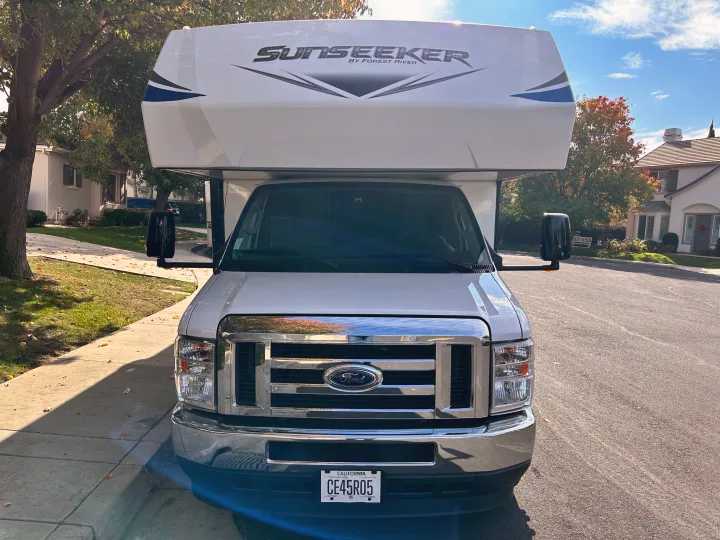 Front view of a white Sunseeker Class C RV rental, built on a Ford chassis, parked on a residential street.. Coachmen Sunseeker 2022