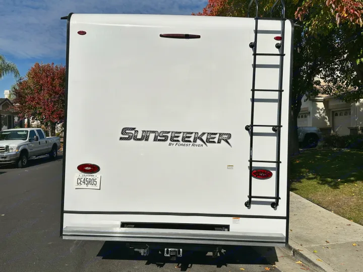 Rear of a white Sunseeker RV rental by Forest River, showing its ladder, lights, and California license plate CE45R05.. Coachmen Sunseeker 2022