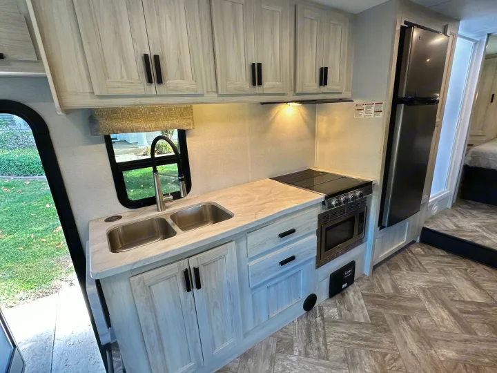 This RV rental features a modern kitchen: light wood cabinets, double sink, stove, microwave, and fridge. Ready for travel.. Coachmen Sunseeker 2022