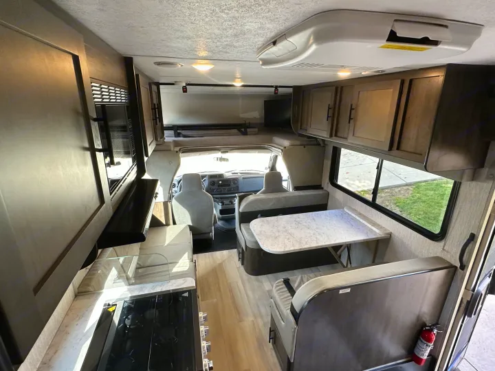 Clean RV rental interior shows kitchen, dinette, and over-cab bunk above the cab. A modern and functional mobile living space.. Coachmen Leprechaun 2022