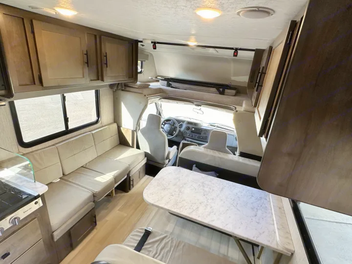 RV rental interior featuring a bright dinette, compact kitchen, and an over-cab bunk for comfortable travel.. Coachmen Leprechaun 2022