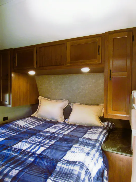This rv rental bedroom features a comfortable bed with blue plaid bedding, pillows, and ample wooden storage.. Jayco Jay Flight 2016