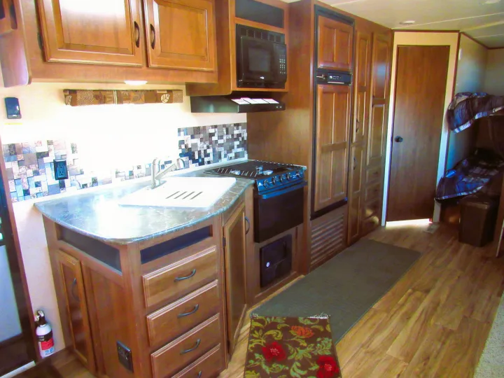 Spacious RV rental kitchen featuring a sink, stove, microwave, and refrigerator, with bunk beds visible in the cozy living area.. Jayco Jay Flight 2016