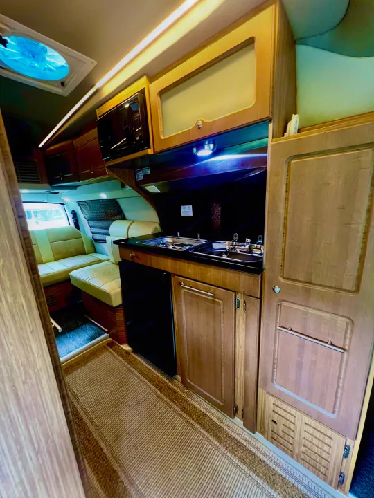 Interior of an RV rental showcasing a compact kitchen with sink, stove, microwave, fridge, and light seating.. Roadtrek Roadtrek Class B 2015