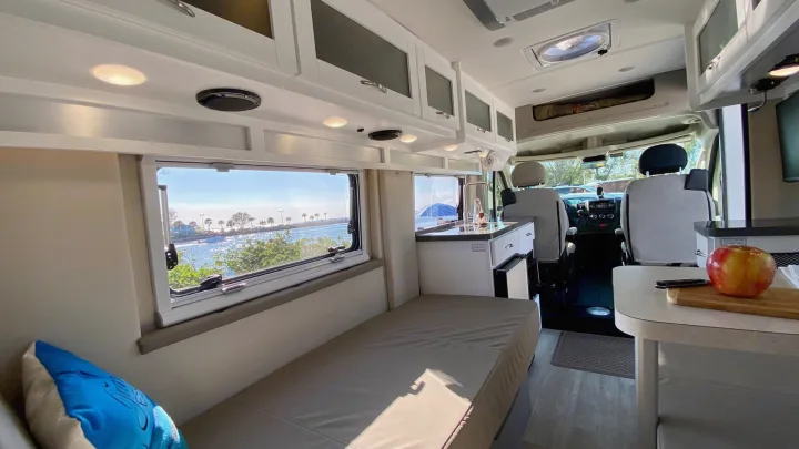 Spacious RV rental interior with bed, kitchenette, and panoramic waterside view from windows.. Coachmen Nova20 Li3.  Lithium / generator free silent power 2022