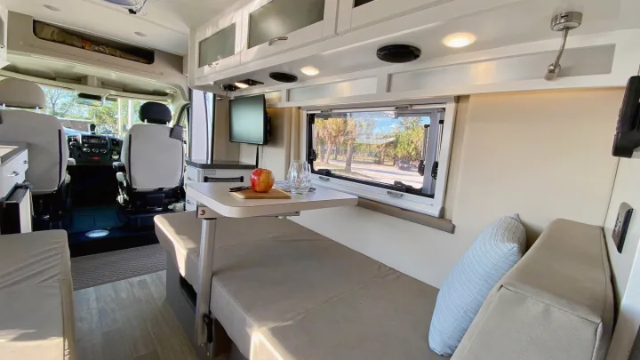 Inside a clean RV rental: dining area, front cab, and comfy seating by a large window. Ideal mobile living.. Coachmen Nova20 Li3.  Lithium / generator free silent power 2022