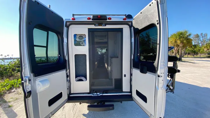 Adventure awaits! This RV rental's rear doors are open, showing its comfy interior & stunning beachside parking spot.. Coachmen Nova20 Li3.  Lithium / generator free silent power 2022