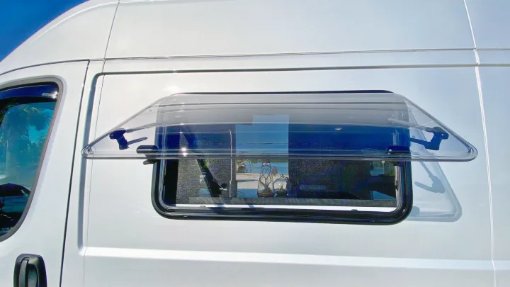 Side of a silver camper van with its transparent, propped-open window revealing a water view. Ideal for an RV rental adventure.. Coachmen Nova20 Li3.  Lithium / generator free silent power 2022