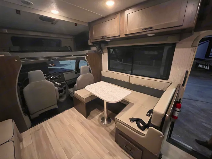 Inside an RV rental: light wood floors, dinette with table, overhead cabinets, and cab-over bunk visible for a comfy journey.. Forest River Coachmen Leprechaun Premier 2022