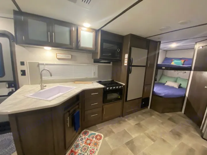 RV rental interior: A modern kitchen with sink, microwave, stove, fridge, and cozy bunk beds. Perfect for family adventures.. Keystone RV CMMM262BH21 2021