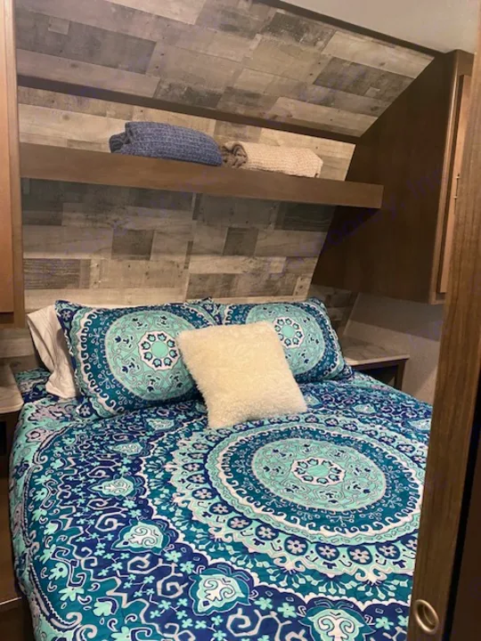 RV rental bedroom featuring vibrant blue and teal mandala bedding, rustic wood paneling, and cozy setup for travel.. Keystone RV CMMM262BH21 2021