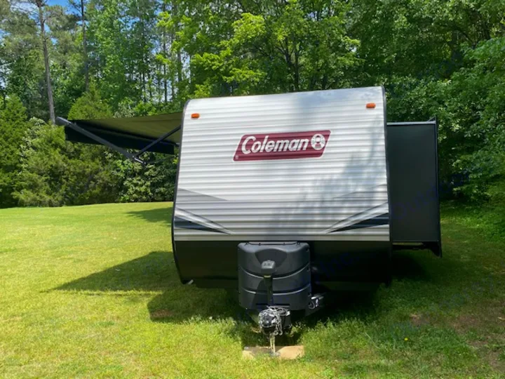 Coleman travel trailer RV rental ready for adventure, parked on green grass with an extended awning.. Keystone RV CMMM262BH21 2021