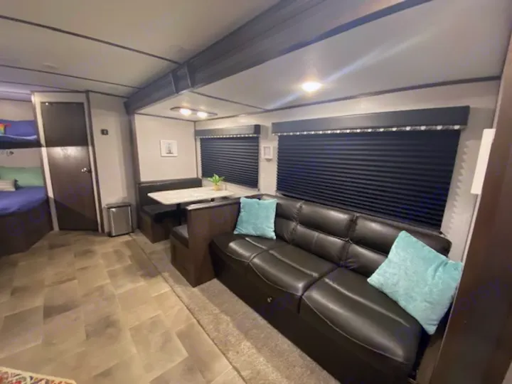 Explore this comfortable rv rental interior: spacious living area with a dark sofa, teal pillows, and functional dinette.. Keystone RV CMMM262BH21 2021