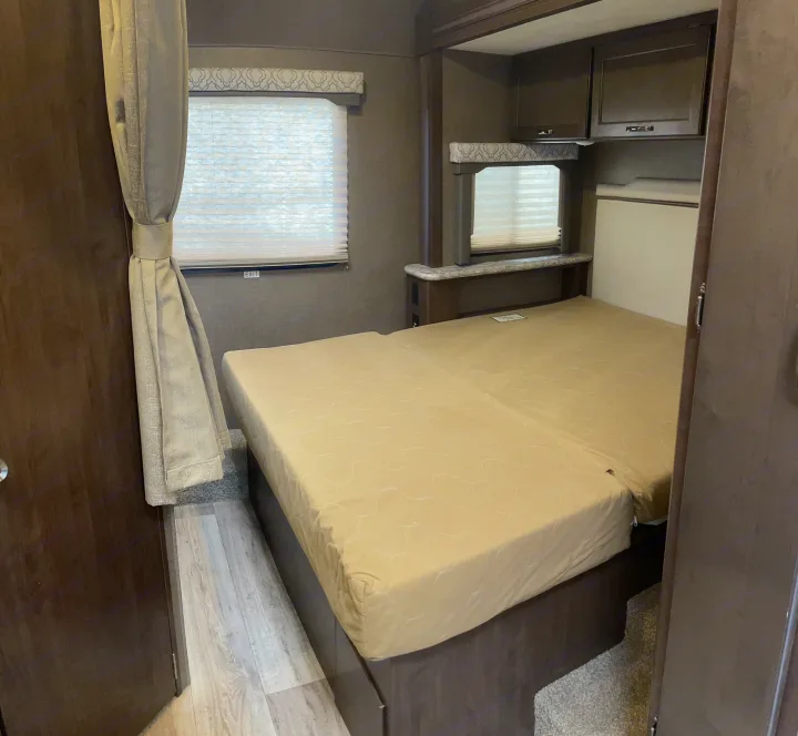 This rv rental features a cozy bedroom with a large bed, windows with blinds, and overhead storage cabinets.. Thor Motor Coach Freedom Elite 2019