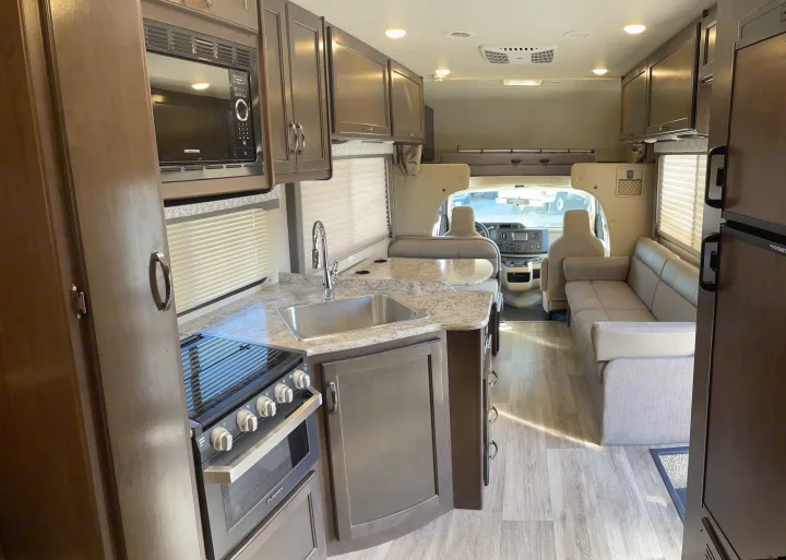 RV rental interior: A well-equipped kitchen with a stove, microwave, and sink, plus a comfortable living area with sofa.. Thor Motor Coach Freedom Elite 2019