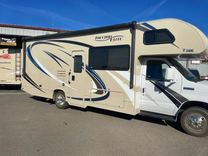 A Thor Freedom Elite Class C RV rental in tan/white/blue, parked at a sales office, ready for your next road trip.. Thor Motor Coach Freedom Elite 2019