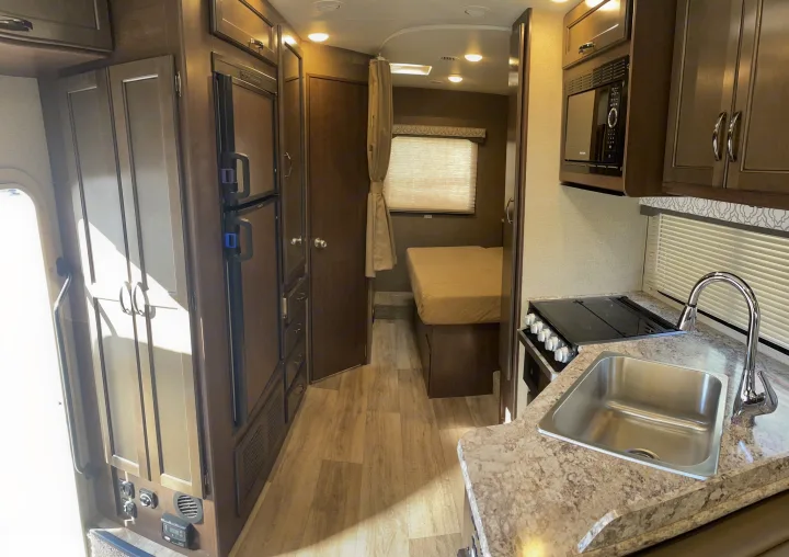 This rv rental showcases a compact interior: kitchen with sink, stove, microwave; refrigerator; and bedroom down the hall.. Thor Motor Coach Freedom Elite 2019